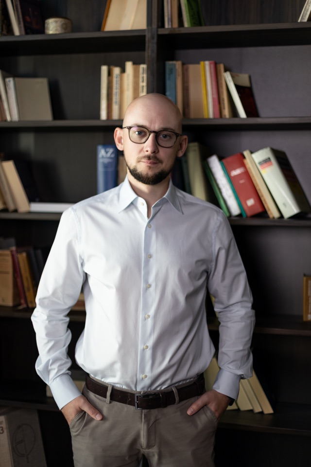 Jędrzej Anuszkiewicz-Michałek na tle regału z książkami